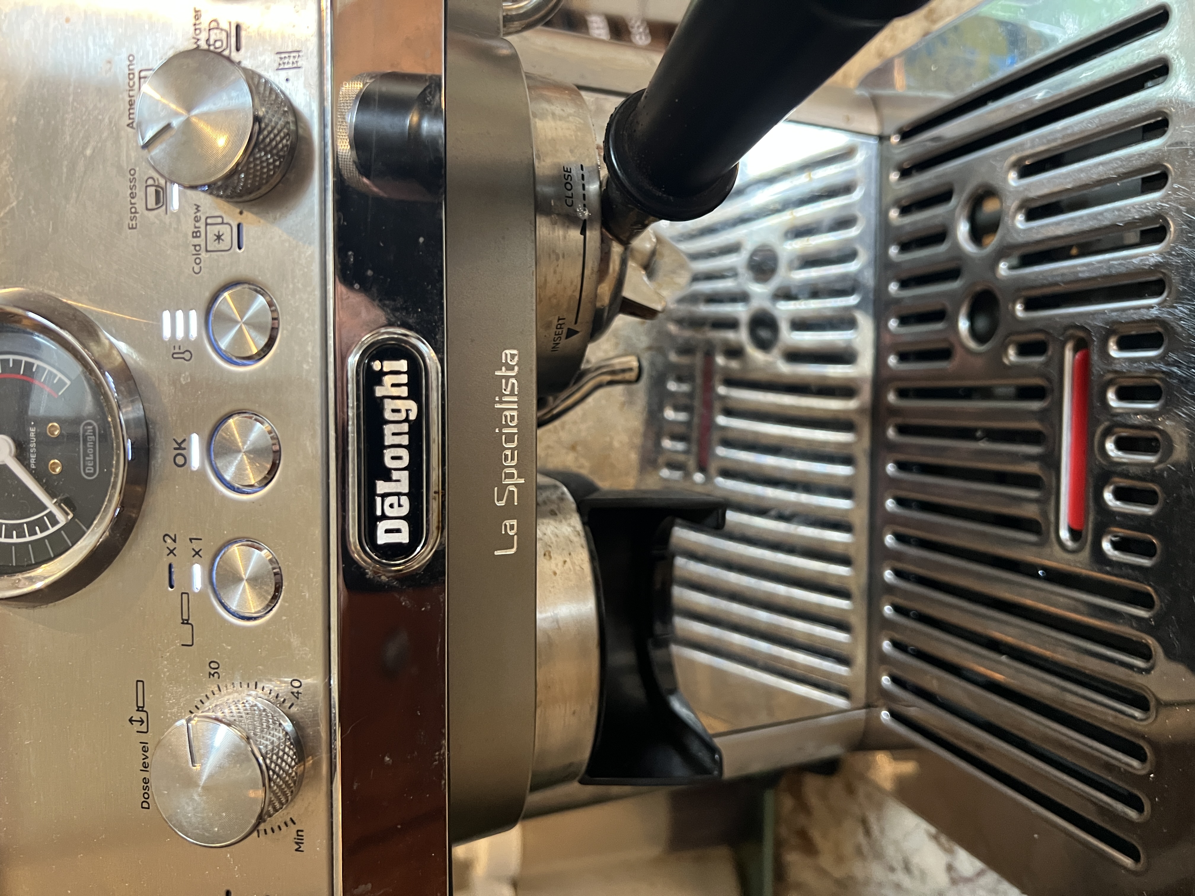 HERO · Detail of the DeLonghi La Specialista Arte Evo EC9255M with the portafilter locked into the brew head (rotated to CLOSE position, INSERT arrow visible above). 'La Specialista' engraved in the stainless steel body to the right of the DeLonghi badge. Mode dial labels visible at top-left (Espresso · Americano · Cold Brew · Water), OK button + x1/x2 shot buttons + dose-level dial (20-30-40 markings) on the control face. Pressure gauge edge at lower-left.