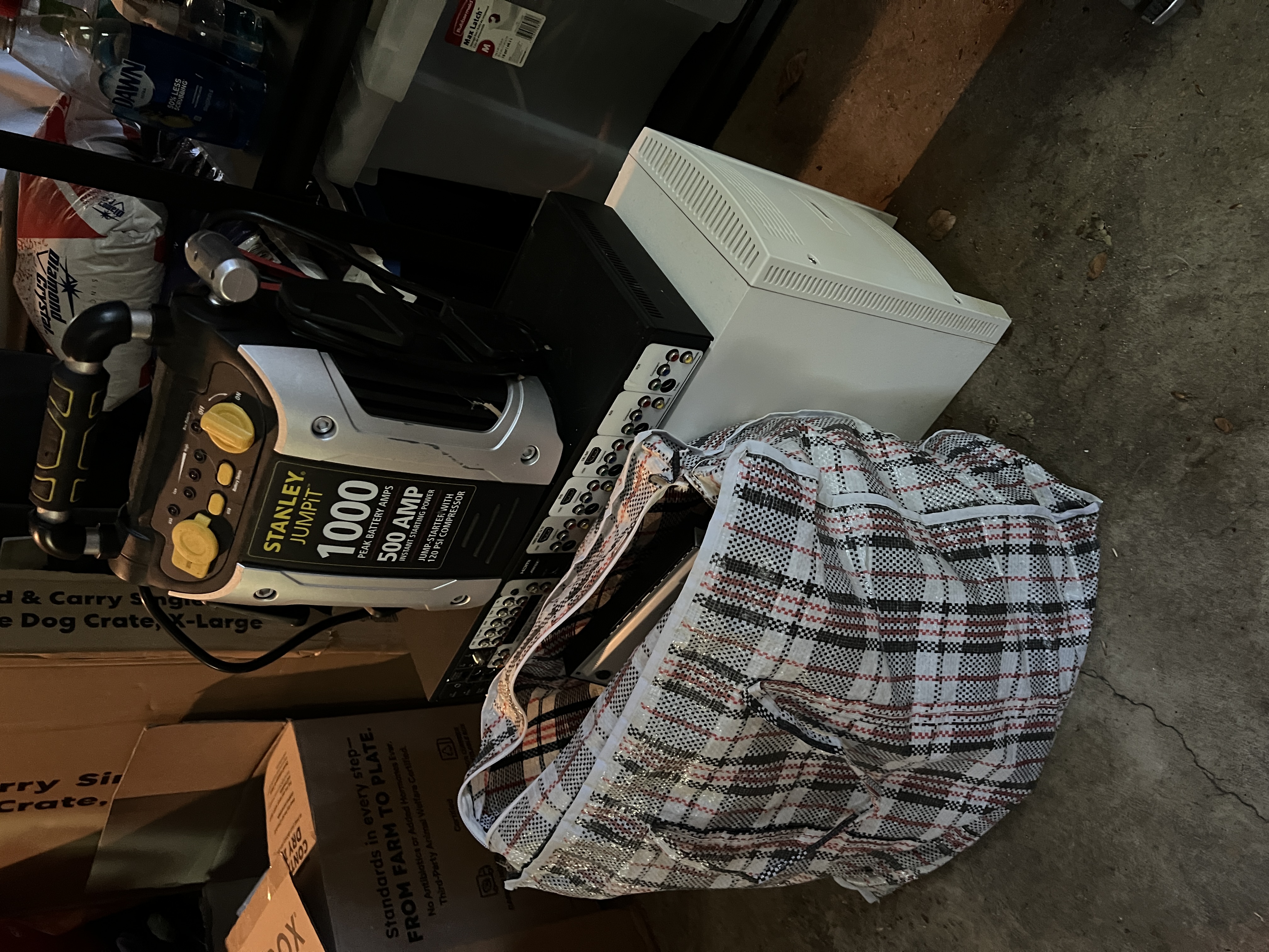 Electronics lot in garage including desktop PC tower, Stanley Jump-It battery pack, and bagged items for e-waste pickup.