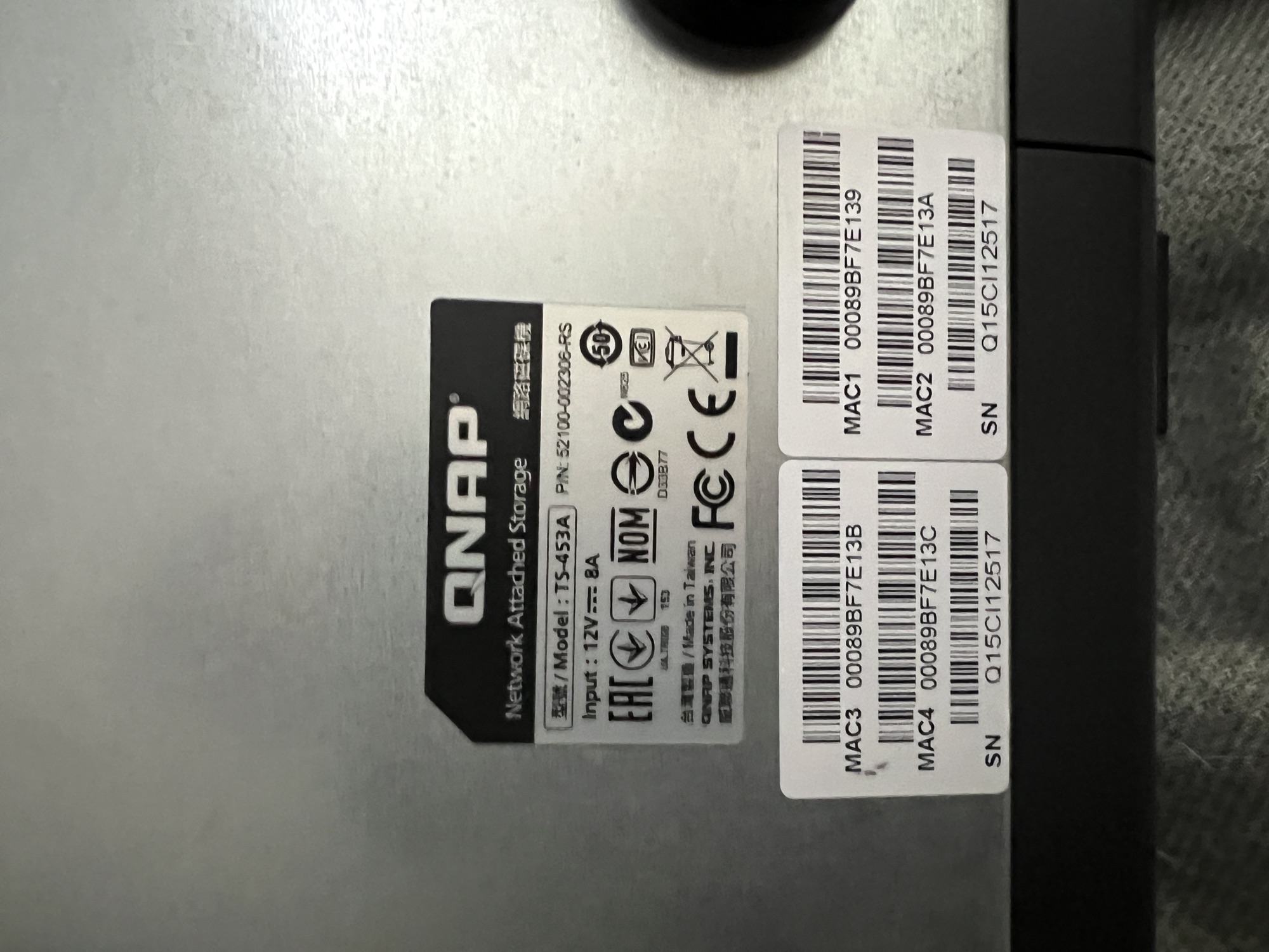 QNAP TS-453A rear rating plate — model TS-453A, part number 52100-002306-RS, 12 V 8 A input, certification marks (CE / FCC / NOM / EAC), and the four sequential MAC-address stickers plus serial number Q15CI12517 from a single 2015 production batch.