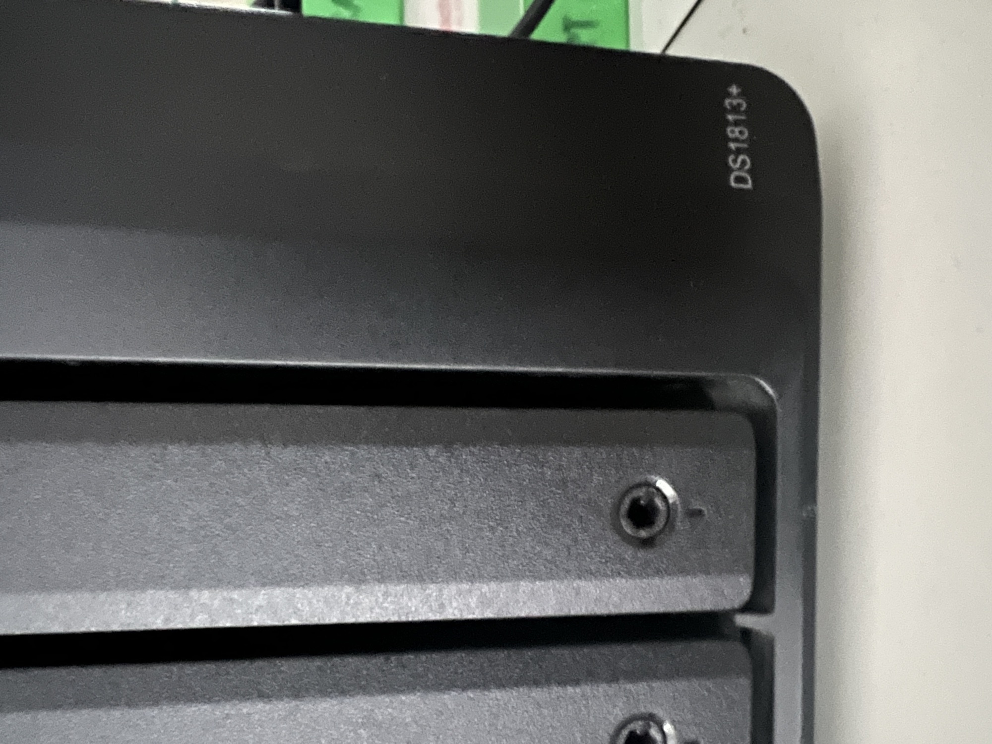Close-up of the Synology DS1813+ model badge etched on the top-front edge of the chassis — definitive model identification, captured 26 May 2026 alongside the front drive-tray latch detail.